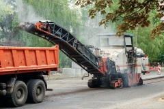 The machine is cutting asphalt, cutting old asphalt with a special machine and loading it into a dumper on a summer day. Repair of roads, replacement of asvalt, construction work.