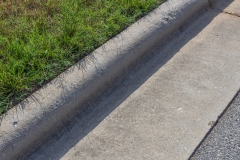 Close view of formed concrete curb, green grass and asphalt, horizontal aspect