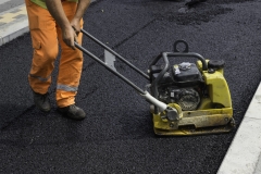 Worker with vibrating compactor plate in action